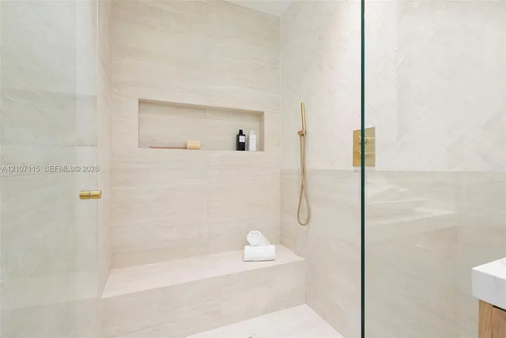 Walk-in shower featuring herringbone-patterned tile wall accents, built-in bench seating, recessed wall niche, and gold-finish hardware behind a glass enclosure
