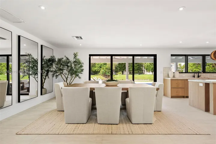 Open-concept interior featuring large-format tile flooring, recessed ceiling lighting, wall-to-wall mirrors, and multi-panel sliding glass doors opening to a covered patio
