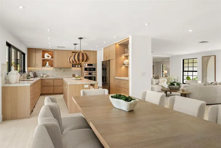 Custom wood cabinetry with integrated lighting, stone countertops, stainless steel built-in double ovens, recessed lighting, and large-format tile flooring
