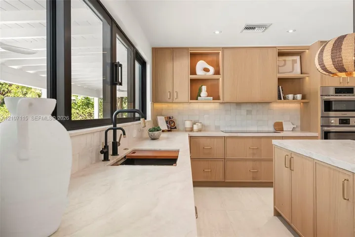 Kitchen featuring light wood-finish cabinetry, stone countertops, square-tile backsplash, matte black faucet, and built-in stainless steel double oven