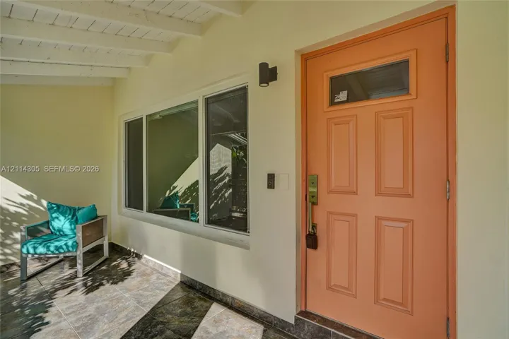 Covered front porch with tile flooring, four-panel entry door with an upper glass insert, and large multi-pane window