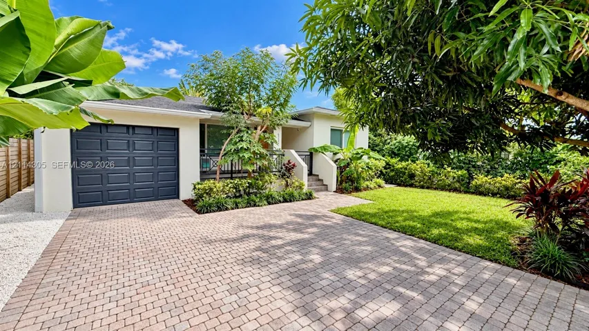 Stucco exterior featuring a paver driveway, single-car garage, manicured lawn, and mature landscaping