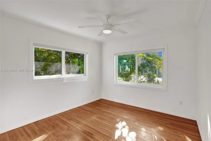 Room featuring wood-finish flooring, dual windows, crown molding, and a central ceiling fan with integrated lighting