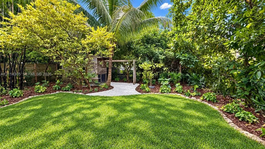 Backyard featuring a manicured lawn, stone-paved walkway, pergola, mature landscaping, and wood-slat perimeter fencing