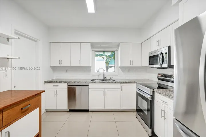 Kitchen featuring white shaker-style cabinetry, stone-finish countertops, subway tile backsplash, stainless steel appliances, and large-format tile flooring