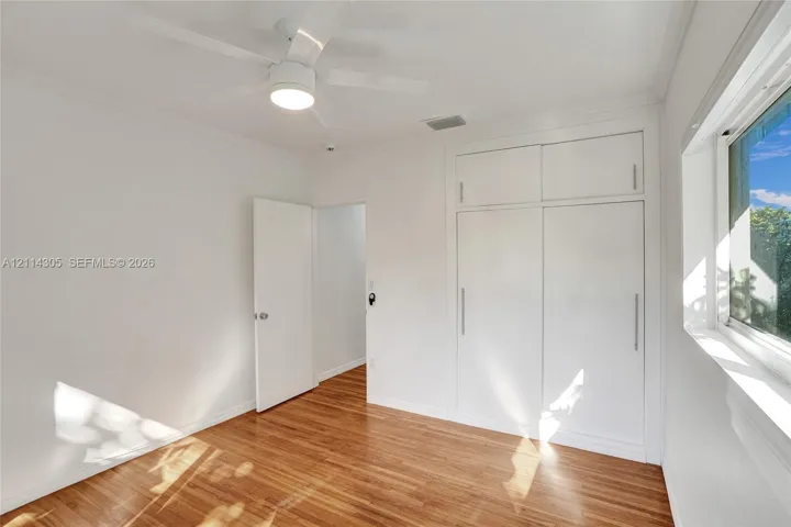 Wood-finish flooring, white built-in floor-to-ceiling cabinetry with vertical hardware, and a ceiling fan with integrated lighting