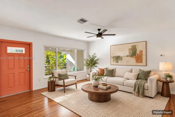 Living area featuring wood-finish flooring, a large picture window, a central ceiling fan with integrated lighting, and a solid-panel door with a glass inlay