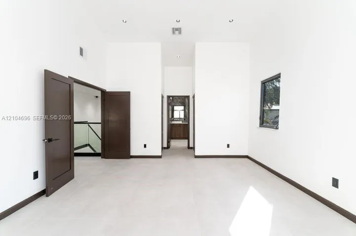 High-ceilinged room featuring large-format tile flooring, dark-toned interior doors, recessed lighting, and expansive window with dark framing