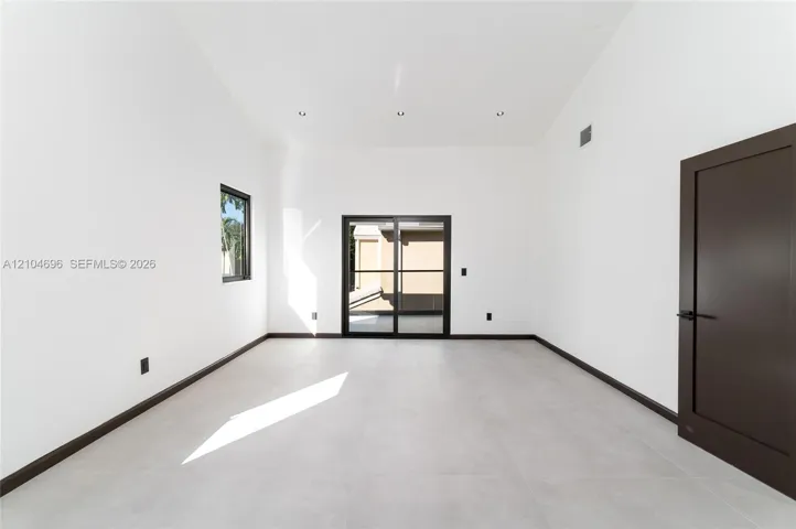 High-ceiling interior featuring large-format tile flooring, recessed lighting, dark-framed sliding glass doors, and a solid-core door with matte black hardware