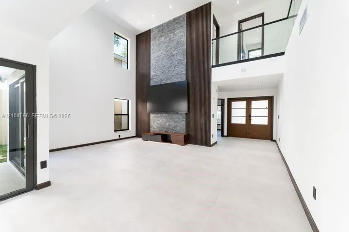 Double-height living area featuring a stone-clad fireplace accent wall, vertical wood-slat detailing, large-format tile flooring, and a glass-paneled mezzanine railing