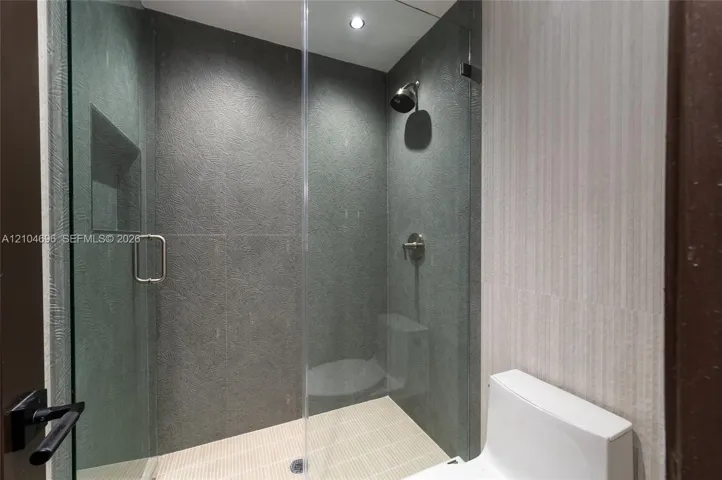 Walk-in shower featuring textured dark stone-style wall tile, frameless glass enclosure, built-in recessed wall niche, and integrated rainfall showerhead