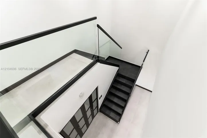 Staircase featuring dark-toned treads, glass railings with black metal trim, and a multi-panel door with frosted glass inserts