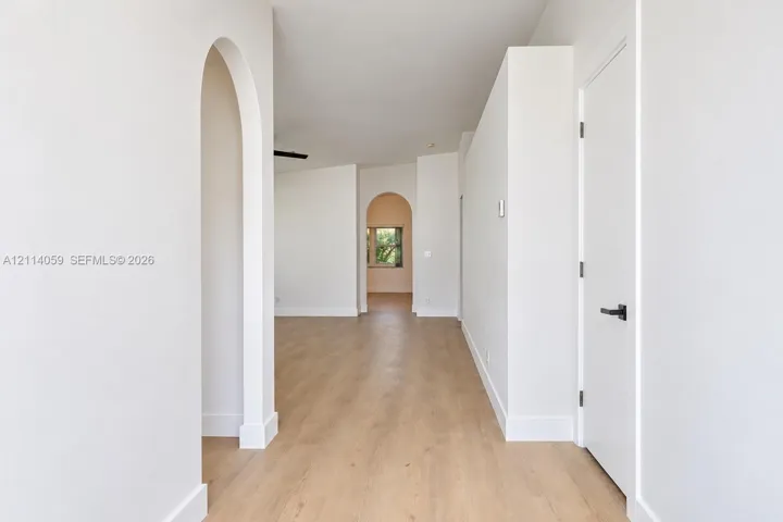 Interior space featuring arched doorways, wood-finish flooring, and minimalist white walls with matte black hardware