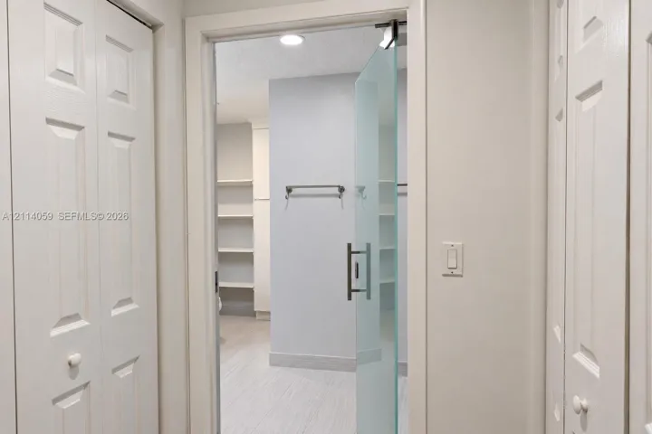 Frameless frosted glass door with a brushed metal handle, recessed ceiling lighting, built-in open shelving, and dual white paneled folding doors
