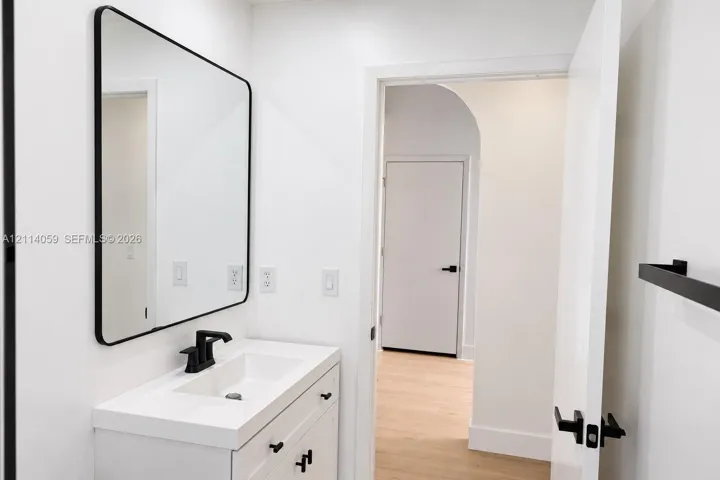 Modern white vanity with a rectangular sink, matte black faucet, rounded rectangular mirror, and matte black hardware featuring an arched doorway entry