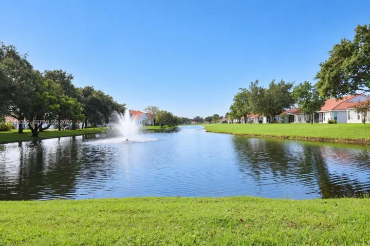 Waterfront setting featuring a central fountain, manicured lawn, and mature canopy trees