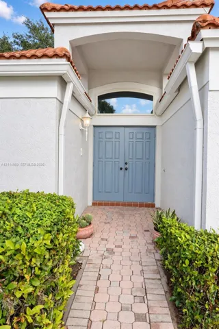 Stucco exterior entryway featuring a terracotta tile roof, arched transom window, dual panel doors, and a decorative wall-mounted lantern