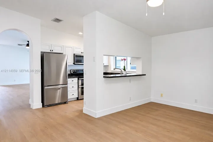 Kitchen featuring stainless steel appliances, white cabinetry, dark stone-finish countertops, and wood-finish flooring, complemented by an arched doorway