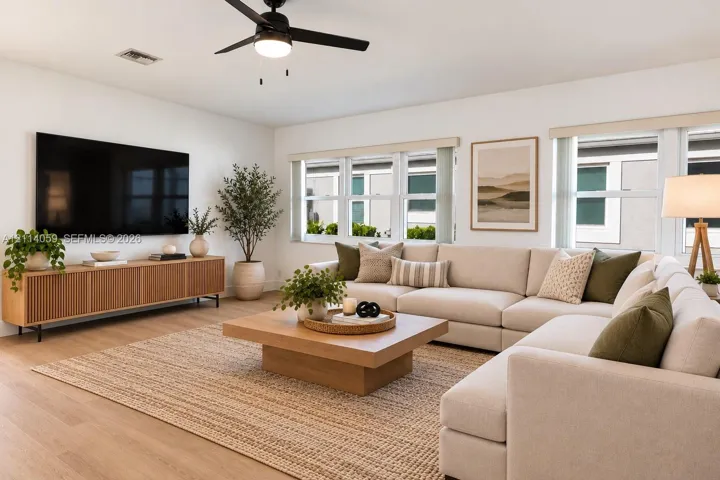 Living area featuring wood-finish flooring, matte black ceiling fan with integrated lighting, neutral wall palette, and expansive multi-pane window configuration
