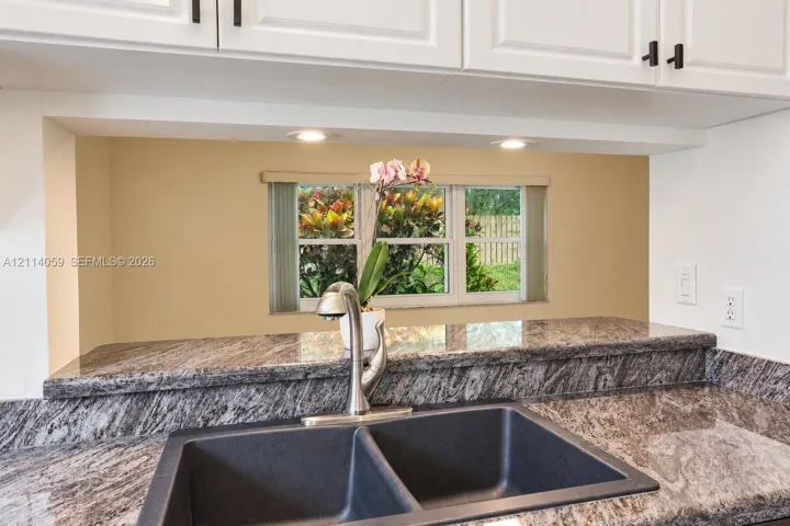 Kitchen featuring stone-finish countertops, undermount double-basin sink, high-arch faucet, white cabinetry with matte black hardware, and recessed lighting