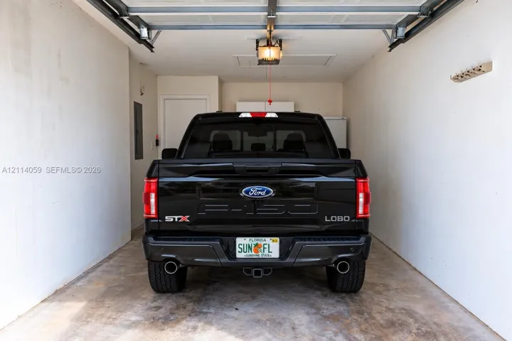 Enclosed garage featuring concrete flooring, a motorized overhead door system, ceiling-mounted light fixture, and interior access door