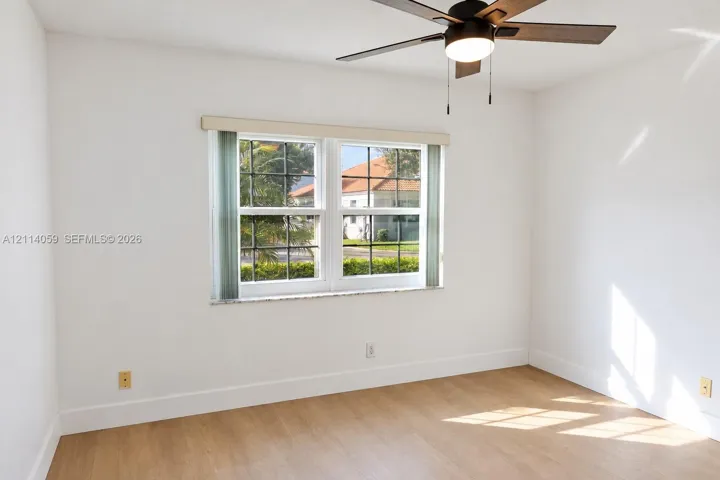 Room interior featuring wood-finish flooring, white walls, dual-pane windows with muntins, and a ceiling fan with integrated lighting
