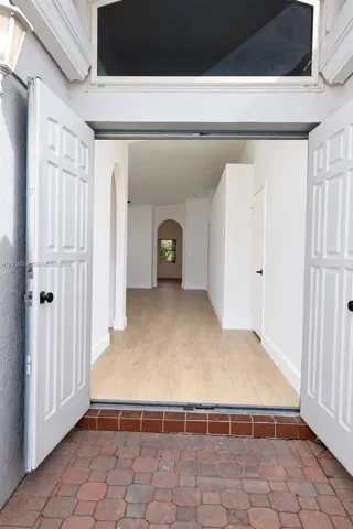 Double front entry doors with transom window, wood-finish flooring, and arched interior doorways