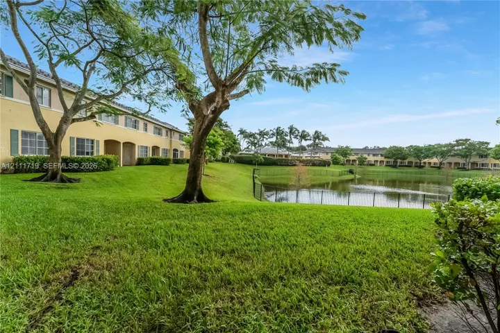 Waterfront grounds featuring a manicured lawn, mature trees, and perimeter fencing
