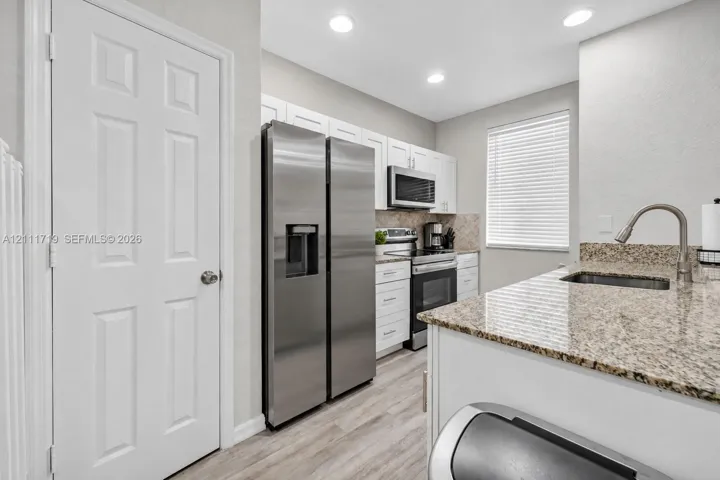 Kitchen featuring white cabinetry, stone countertops, stainless steel appliances, and wood-finish flooring