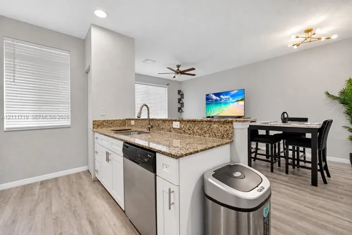 Kitchen featuring a peninsula with stone-finish countertops, white cabinetry, a stainless steel dishwasher, an undermount sink with a gooseneck faucet, and wood-finish flooring
