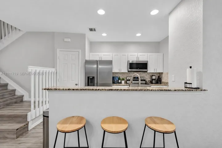Kitchen featuring white shaker-style cabinetry, stone-finish countertops, stainless steel appliances, a breakfast bar, and recessed lighting