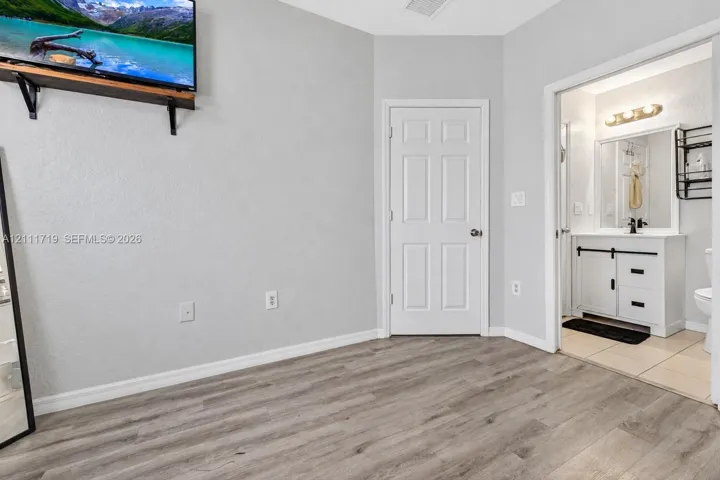 Wood-finish flooring, six-panel interior door, white vanity cabinet with matte black hardware, and rectangular vanity mirror with three-bulb light fixture