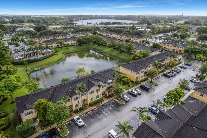 Aerial perspective of multi-unit residential buildings featuring dark tile roofing, stucco exterior walls, mature perimeter landscaping, and a central water feature