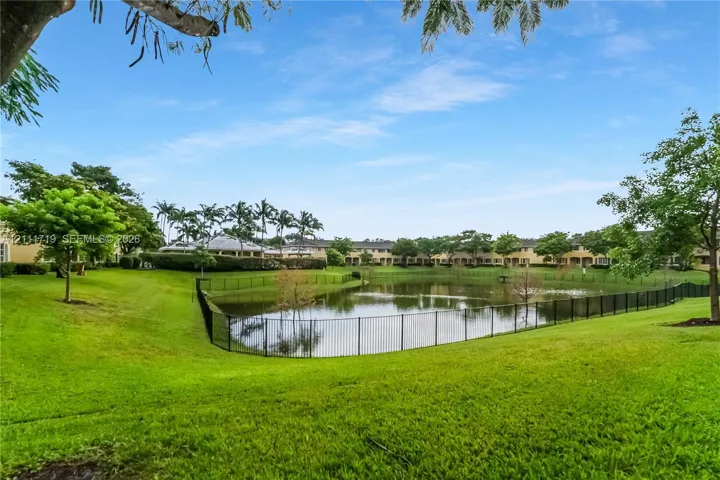 Expansive green space featuring a retention pond, metal perimeter fencing, and mature trees