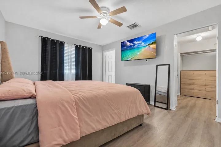 Bedroom featuring wood-finish flooring, a ceiling fan with integrated lighting, and a walk-in closet with built-in shelving