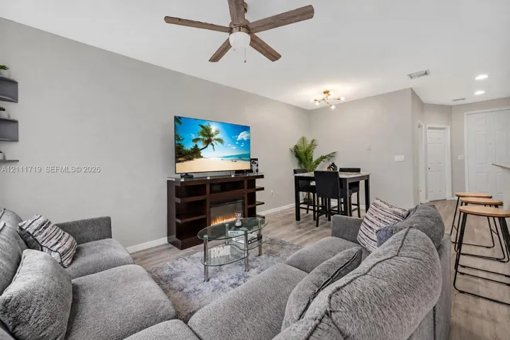 Wood-finish flooring, ceiling fan with integrated lighting, modern multi-arm chandelier, and built-in wall shelving