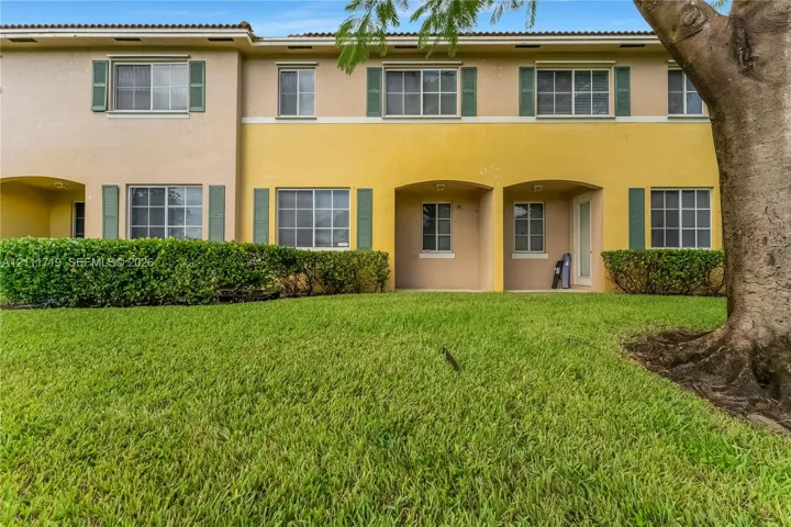 Two-story stucco exterior featuring covered ground-level patios, decorative window shutters, and a manicured​​‌​​​​‌​​‌‌​‌‌​​​‌‌​‌​‌​‌​​​‌​​ lawn