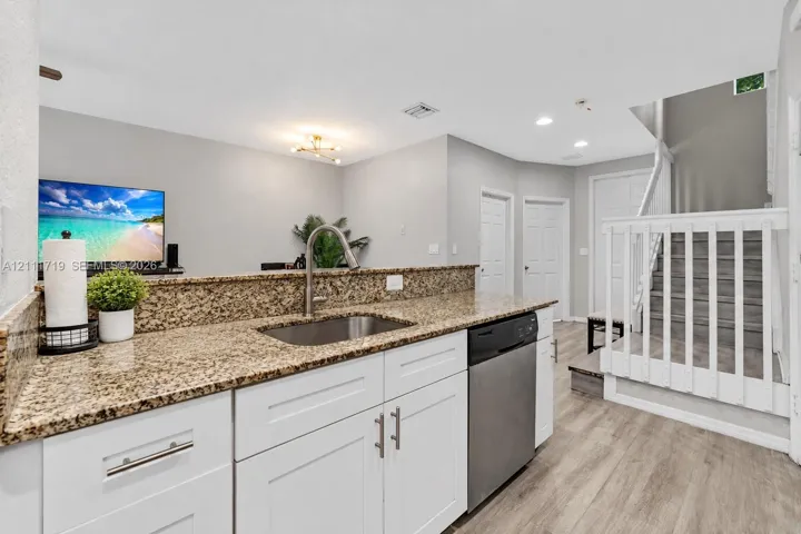Kitchen featuring stone countertops, stainless steel undermount sink, white shaker-style cabinetry, stainless steel dishwasher, and wood-finish flooring
