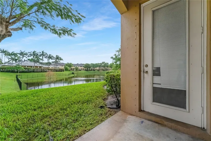 Covered concrete patio featuring a glass-panel door with integrated blinds and direct access to a fenced rear lawn and water feature