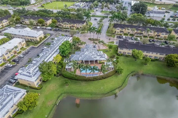 Aerial perspective of a multi-unit property featuring a community swimming pool, concrete-tiled roofing, perimeter landscaping, and waterfront grounds