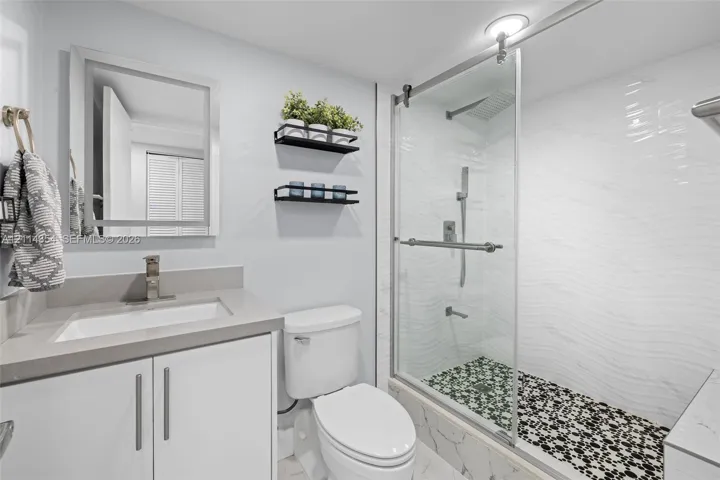Bathroom featuring a vanity with a solid-surface countertop, walk-in shower with sliding glass doors, textured wall tile, and stone-tiled shower floor