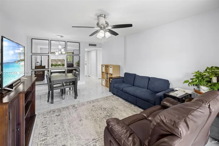 Living area featuring large-format tile flooring, a wall-mounted mirrored panel display, and a ceiling fan with integrated lighting