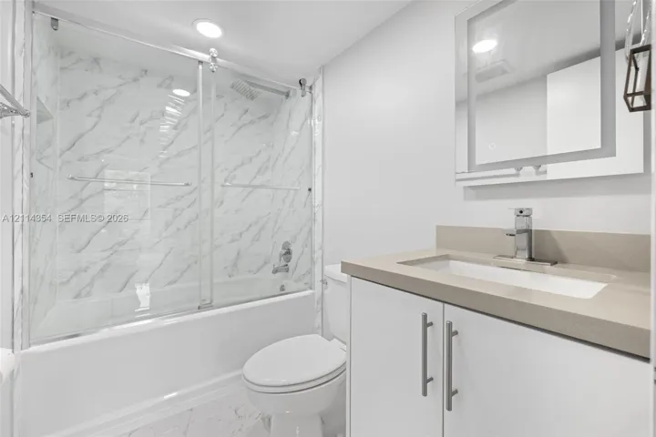 Bathroom featuring a tub-shower combination with floor-to-ceiling stone-pattern tile, a sliding glass door, a vanity with a solid-surface countertop and integrated sink, and a modern rectangular mirror with perimeter integrated lighting