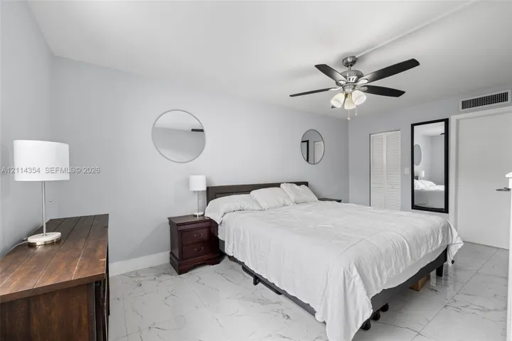 Neutral-toned interior featuring large-format tile flooring, a multi-blade ceiling fan with integrated lighting, and a bi-fold closet door
