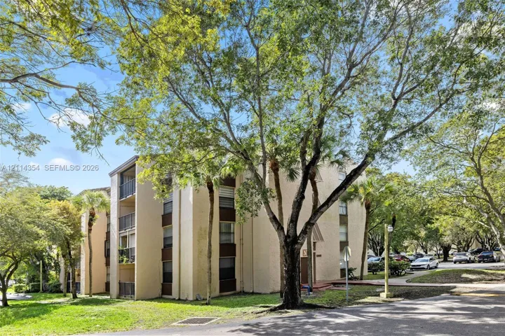 Multi-story exterior featuring a stucco facade, private balconies with metal railings, and mature landscaping