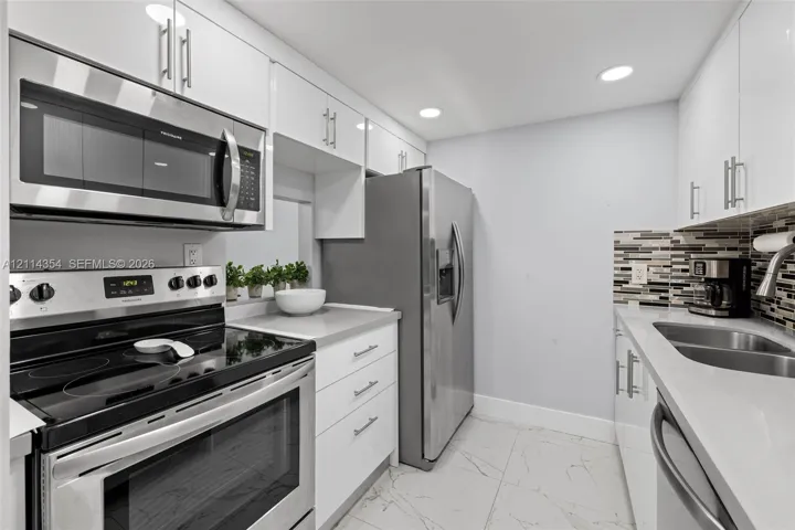 Kitchen featuring white gloss cabinetry, stone-finish countertops, stainless steel appliances, a multi-tone glass tile backsplash, and large-format porcelain tile flooring