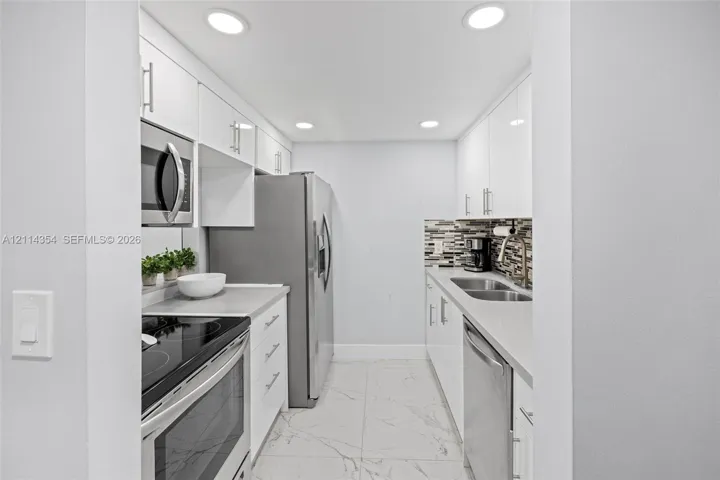 Kitchen featuring white high-gloss cabinetry, stainless steel appliances, quartz countertops, a multi-tone tile backsplash, and large-format tiled flooring