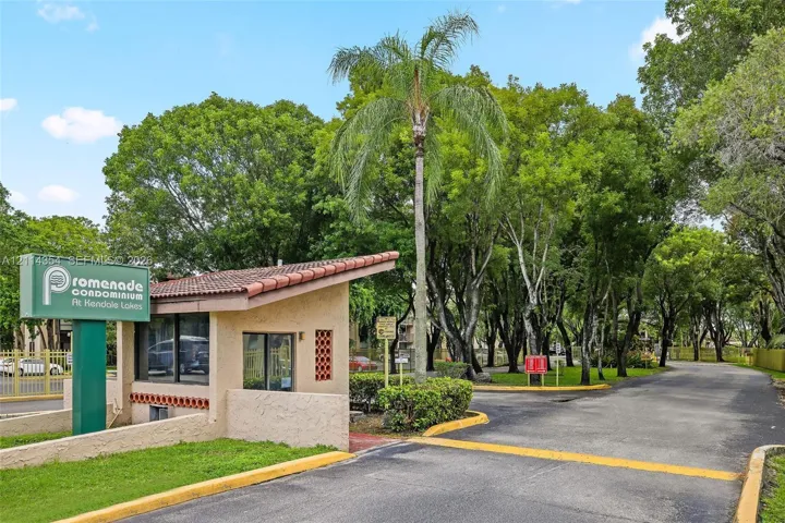 Gated entrance featuring a tile-roofed guardhouse, paved thoroughfare, and mature landscape elements