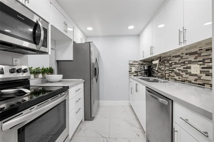 Kitchen featuring white high-gloss cabinetry, stainless steel appliances, multi-tonal linear tile backsplash, solid-surface countertops, and large-format tile flooring