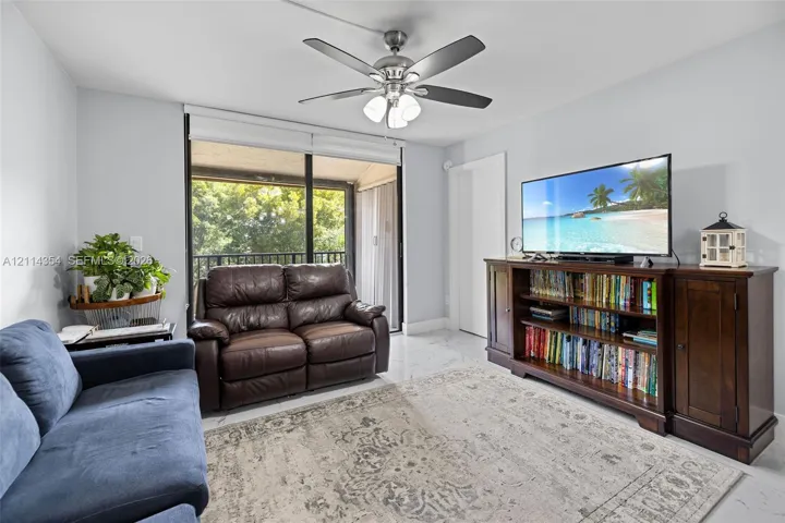 Living area featuring large-format tile flooring, a ceiling fan with integrated lighting, and glass sliding doors providing external access